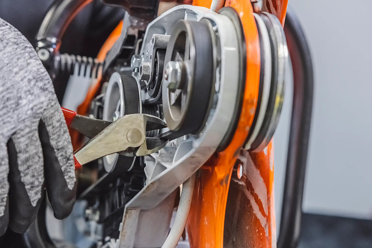 A close-up of a certified STIHL mechanic's gloved hand using a metal tool to adjust or repair a chain drive belt system on an orange and white STIHL TS420 concrete cutter.